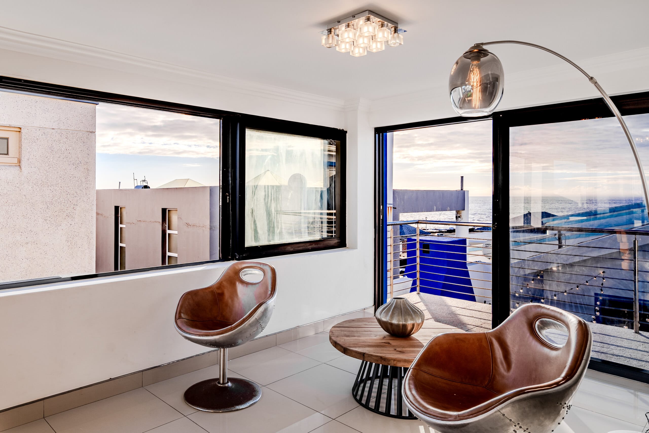 The glass-box dining area at The Lighthouse with tan swivel chairs facing the ocean through full-height windows