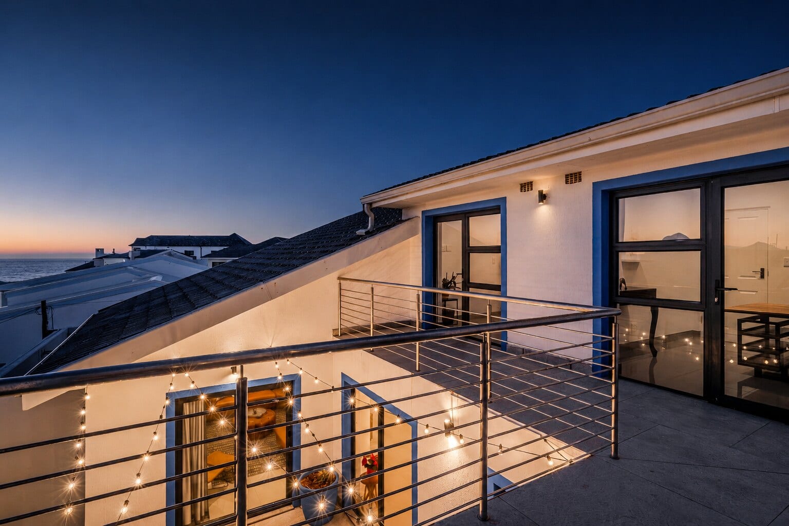 The rooftop terrace at The Lighthouse at twilight, festoon lights on and the Atlantic going dark beyond