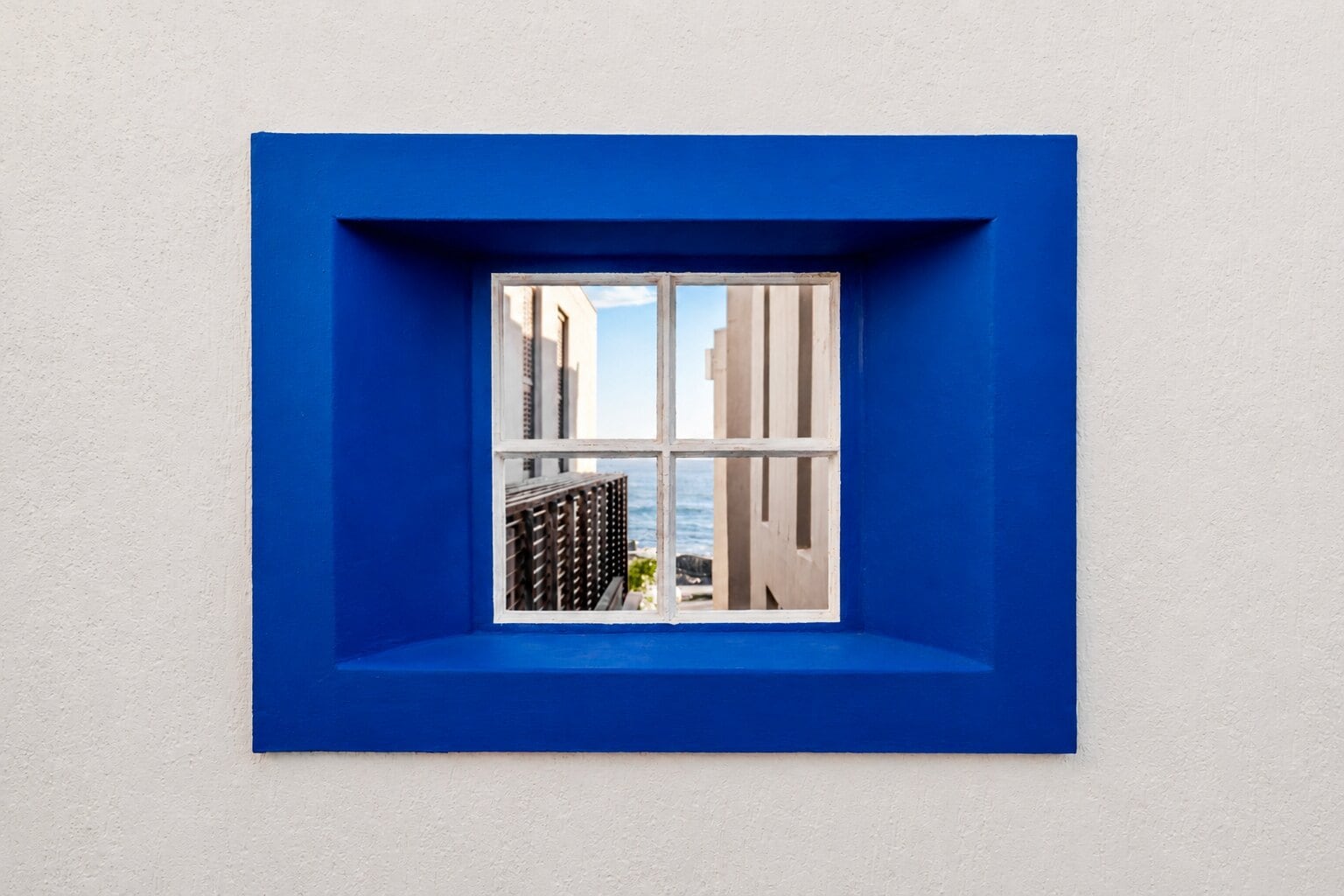 A cobalt-blue framed window at The Lighthouse holding a narrow glimpse of the Atlantic